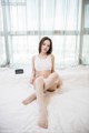 A woman sitting on a bed in a white tank top and fishnet stockings.