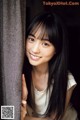 A woman with long black hair leaning against a curtain.