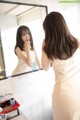 A woman in a white dress looking at herself in the mirror.