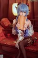 A woman with blue hair sitting on a red couch holding a pan flute.