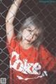 A young girl in a red shirt behind a chain link fence.