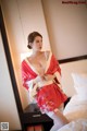 A woman in a red kimono sitting on a bed.