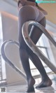 A woman in a white top and black tights leaning against a metal railing.