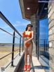 A woman in an orange bikini standing on a balcony.