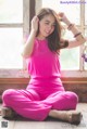 A woman in a pink jumpsuit sitting on the floor.