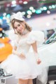 A woman in a white dress standing next to a white car.