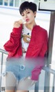 a woman in a red jacket and denim shorts eating an ice cream cone