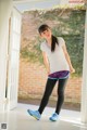 A woman in a white shirt and black leggings standing in front of a door.