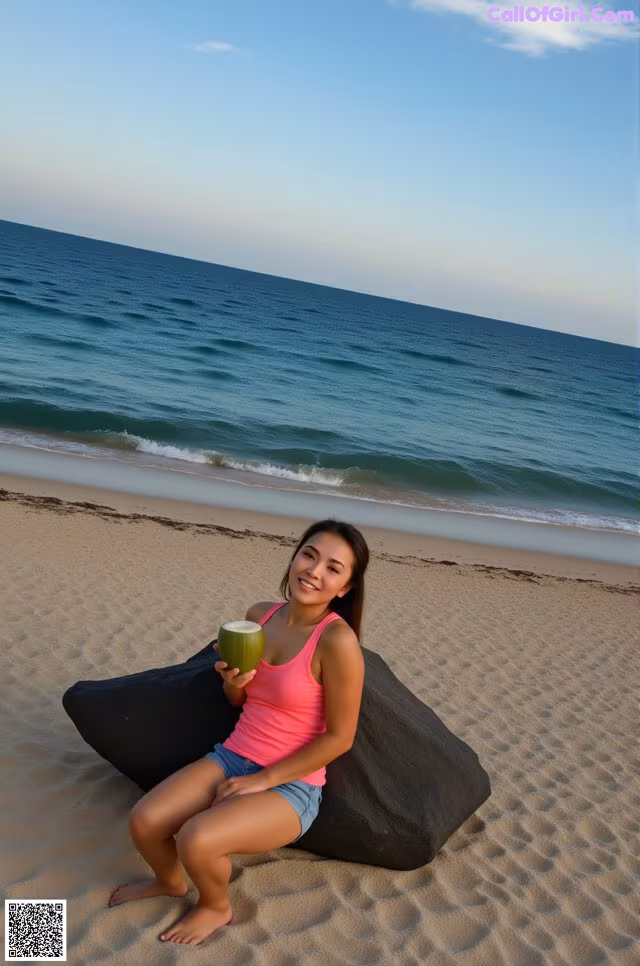 A woman sitting on a bean bag on the beach holding a coconut.