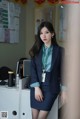 A woman in a blue suit standing in front of a desk.