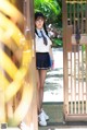 A woman in a school uniform standing in front of a gate.