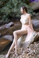 A woman sitting on a rock by a stream.