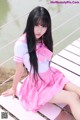 A woman in a pink dress sitting on a wooden bridge.