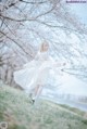 A little girl in a white dress is standing under a tree.