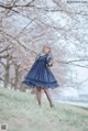 A woman in a blue dress standing in front of a tree.