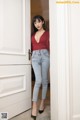 A woman in a red top and jeans standing in front of a door.