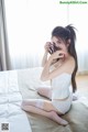 A woman sitting on a bed in a white lingerie.