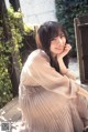 A woman sitting on a wooden bench with her hand on her chin.